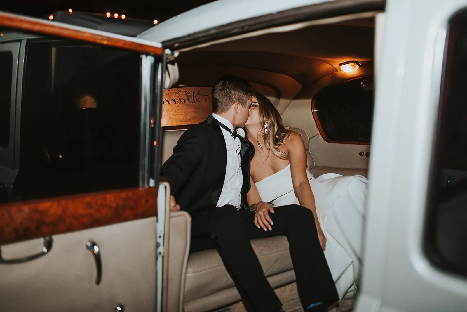 Bride and groom kissing in getaway car after leaving elegant classic wedding