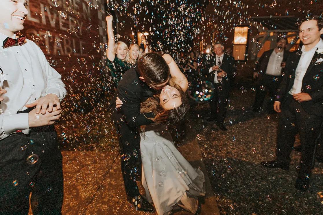 Groom spinning his bride and dipping her to kiss her at their wedding exit as the guests blow bubbles around them