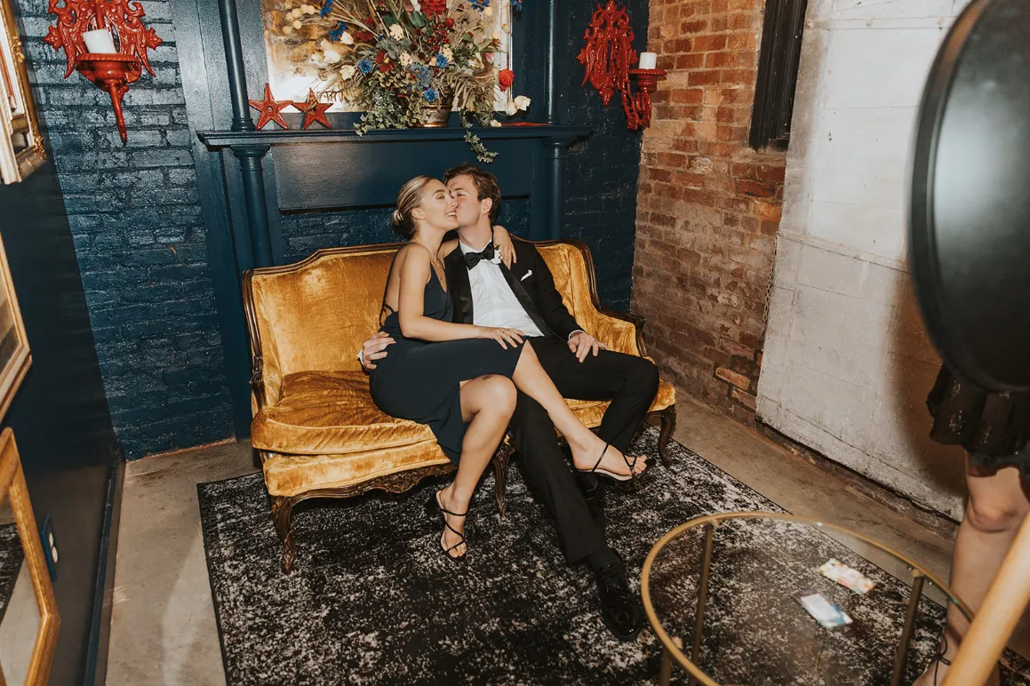 Wedding guests embracing at a reception on a loveseat in a nook room designed to be elegant and rustic