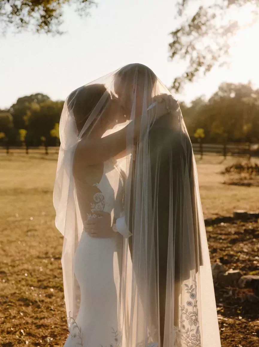 Bride and groom kissing underneath a bridal veil in the rustic Georgia countryside at sunset