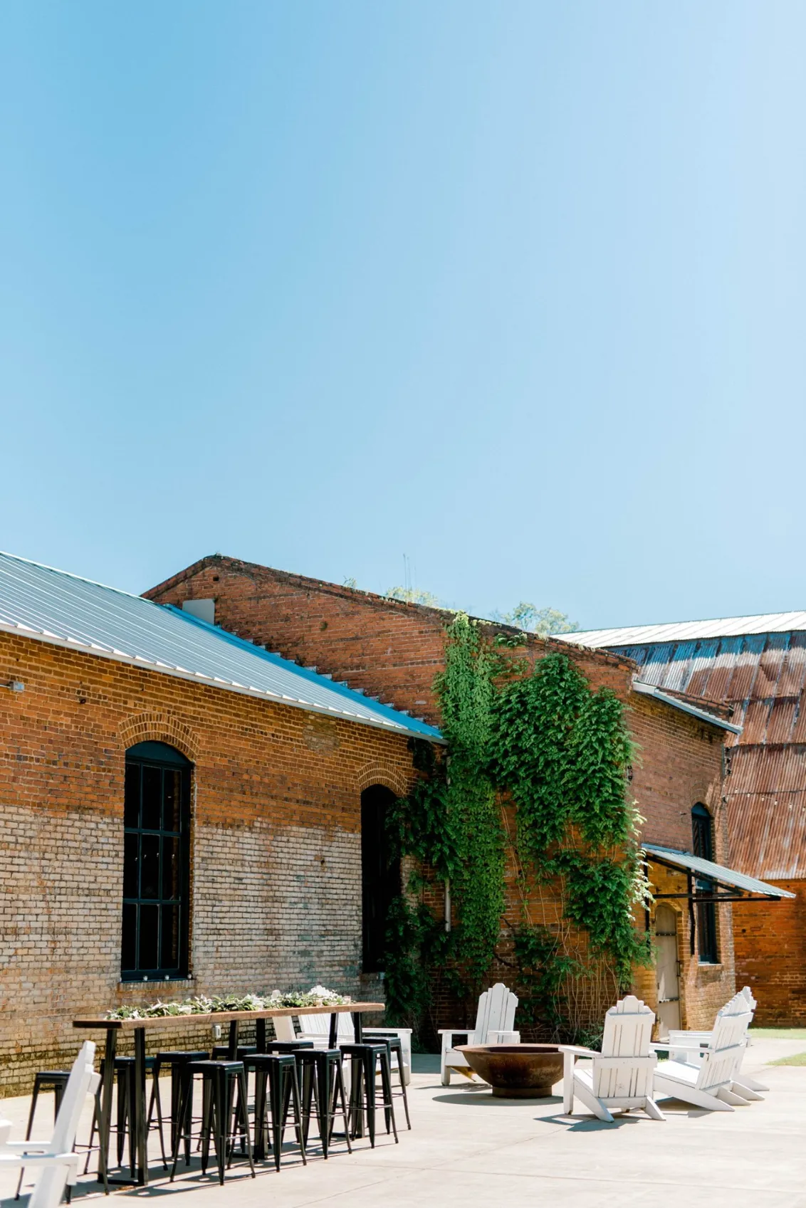 Empire Mills wedding venue back patio outdoor space with rustic table and barstools and Adirondack chairs and fire pit for an outdoor wedding gathering