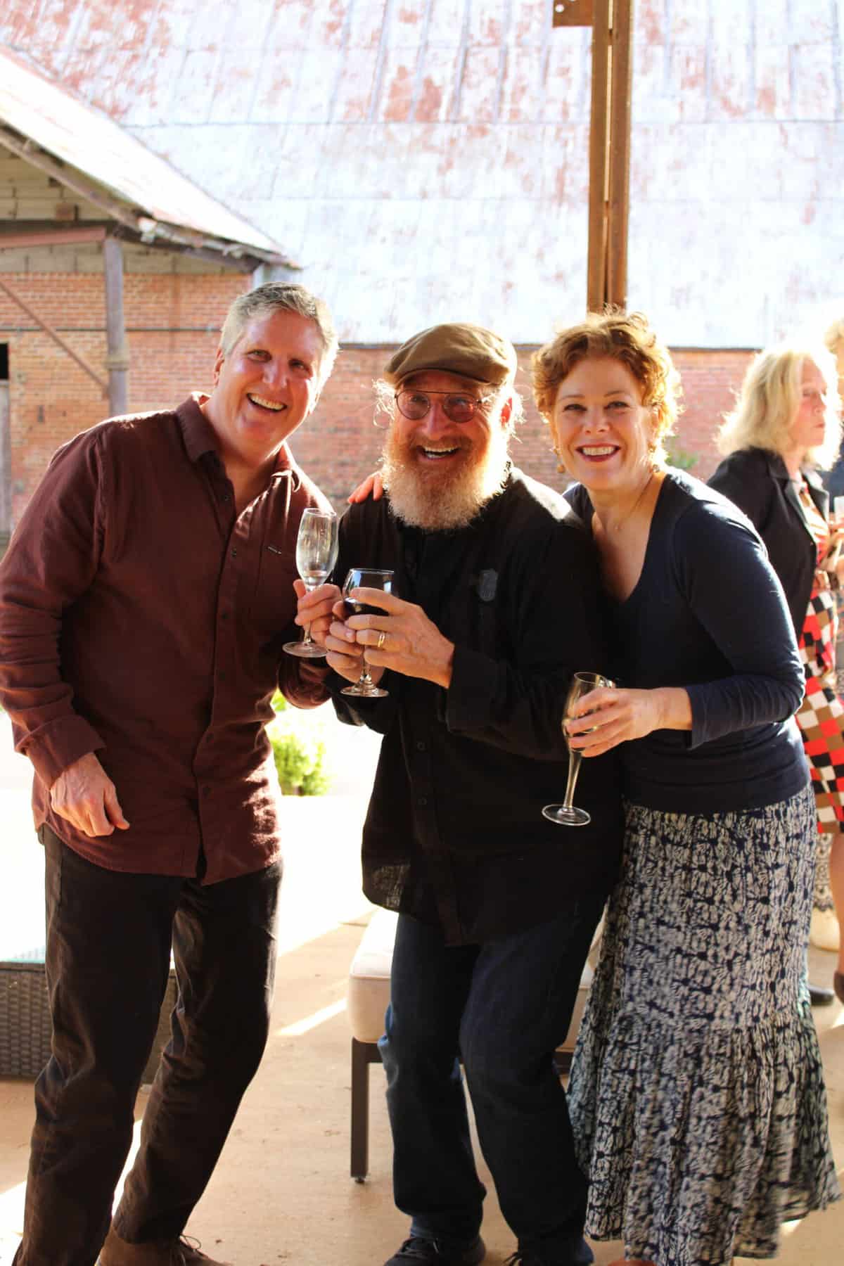 Two men and a woman smiling and posing for a photo holding glasses of champagne at an outdoor social event at Empire Mills