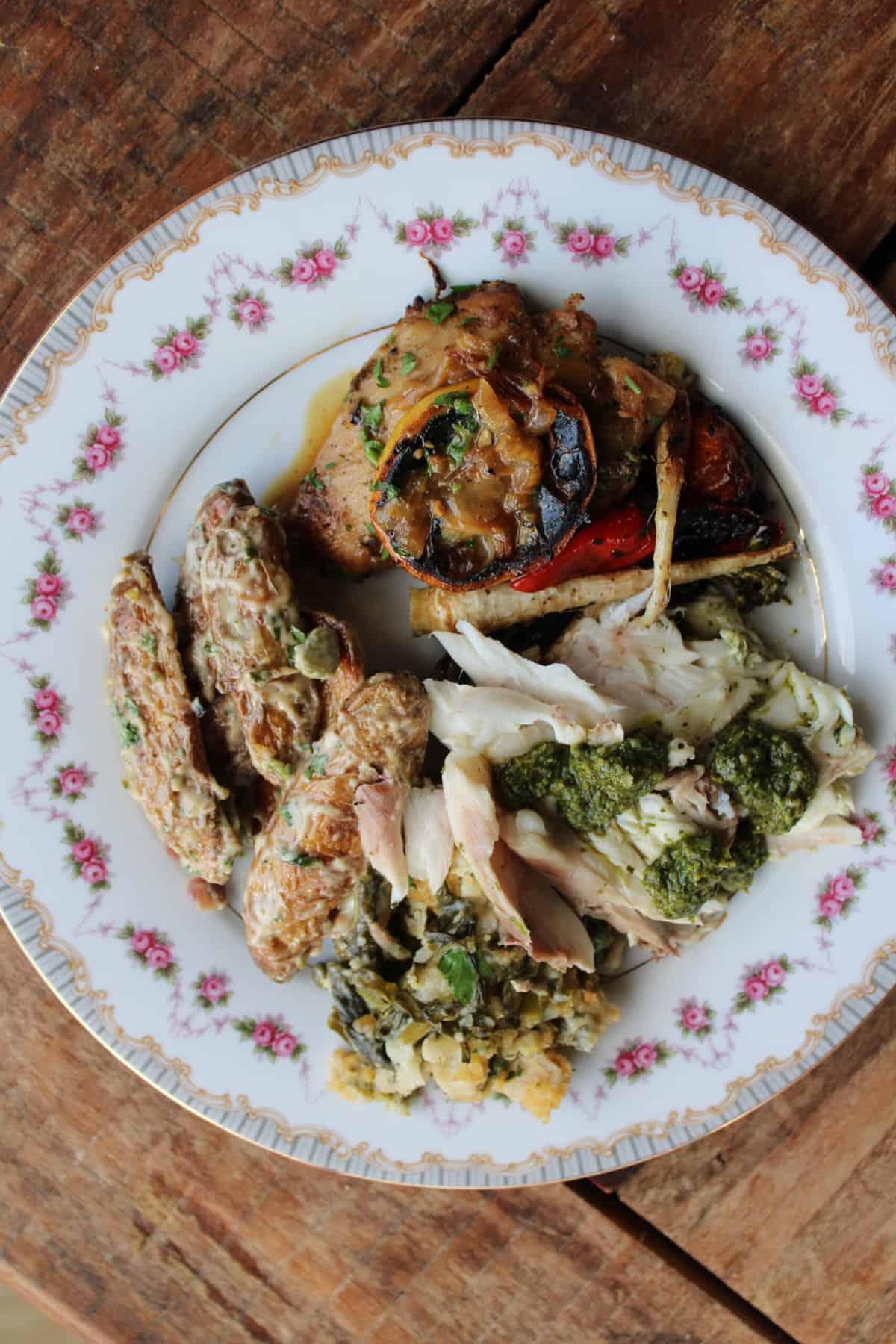 An elegant china plate with a meal of southern comfort food like chicken, pesto, vegetables, and fingerling potatoes