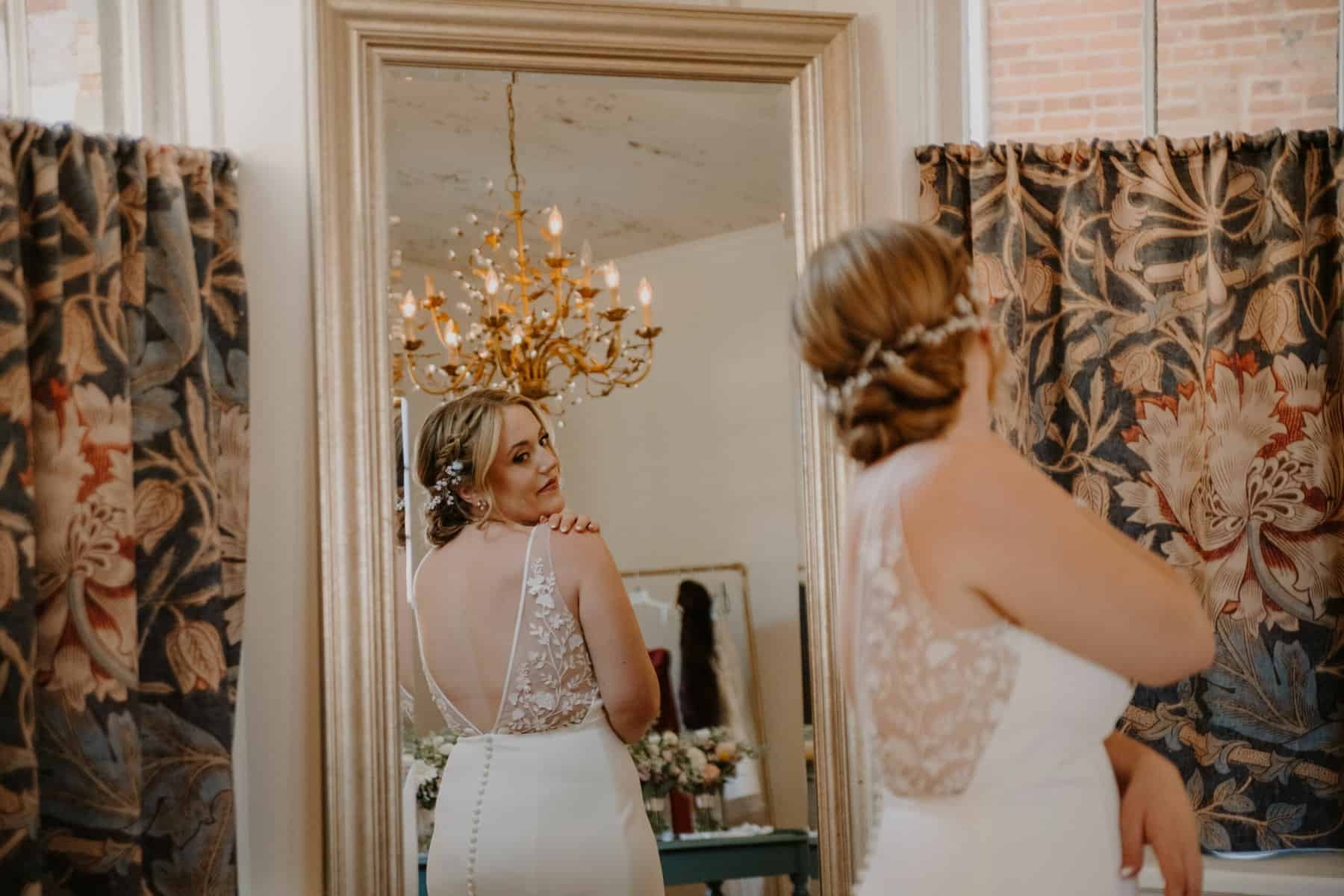 Bride turned around looking at herself in mirror while getting ready for wedding in bridal suite at Empire Mills in Madison, Georgia.