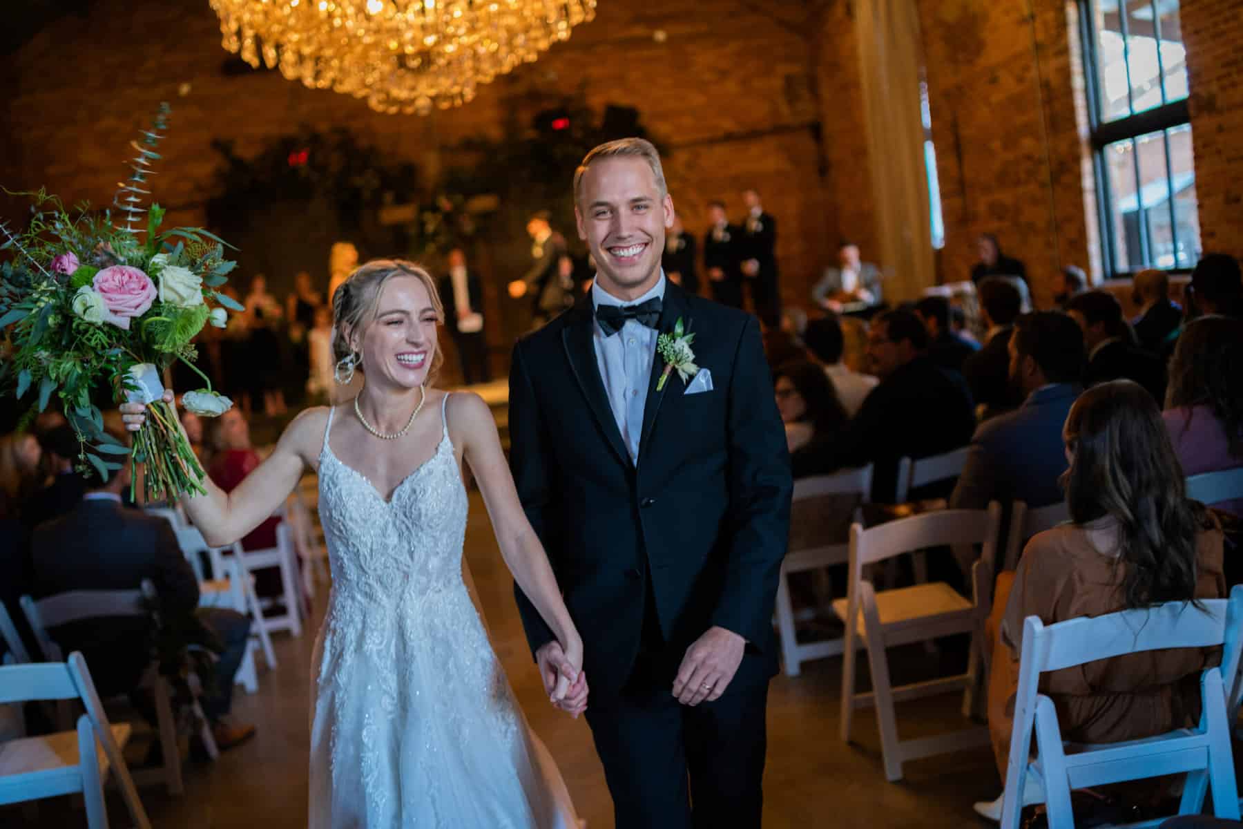 Bride and groom smiling holding hands walking down aisle after getting married at Empire Mills in Madison, Georgia.